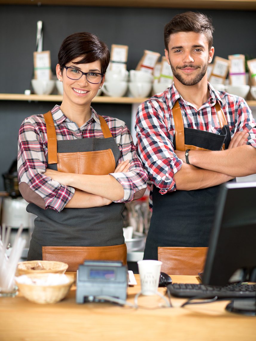 Two friendly baristas standing behind a coffee counter.