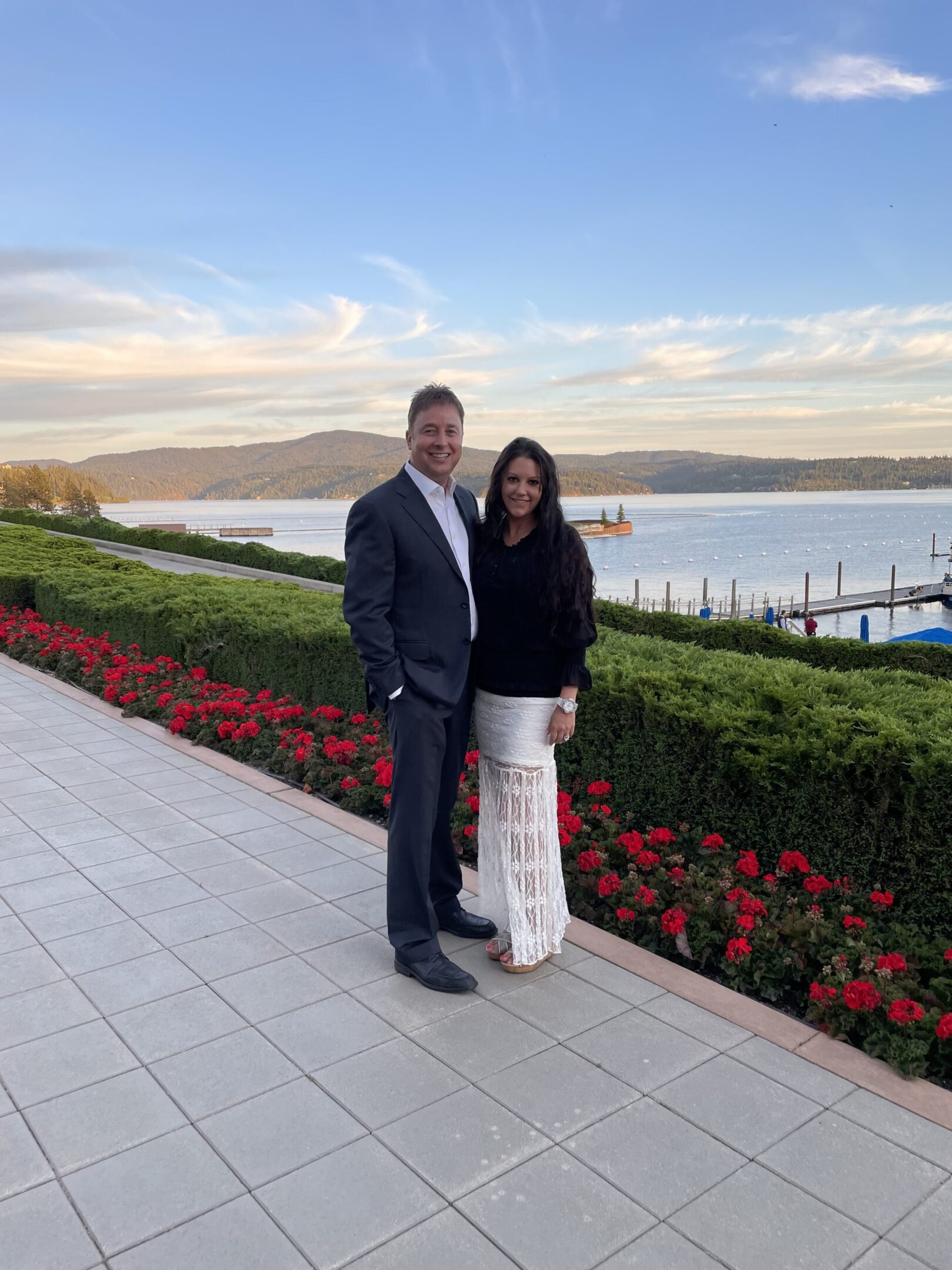 A couple posing outdoors near a waterfront with scenic hills in the background.